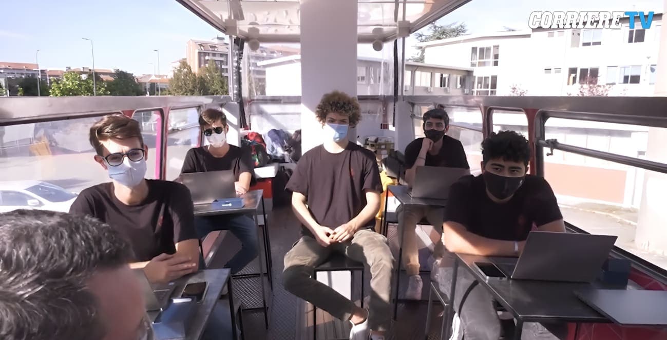 A group of people sitting on top of a bus next to each other with laptops on their laps