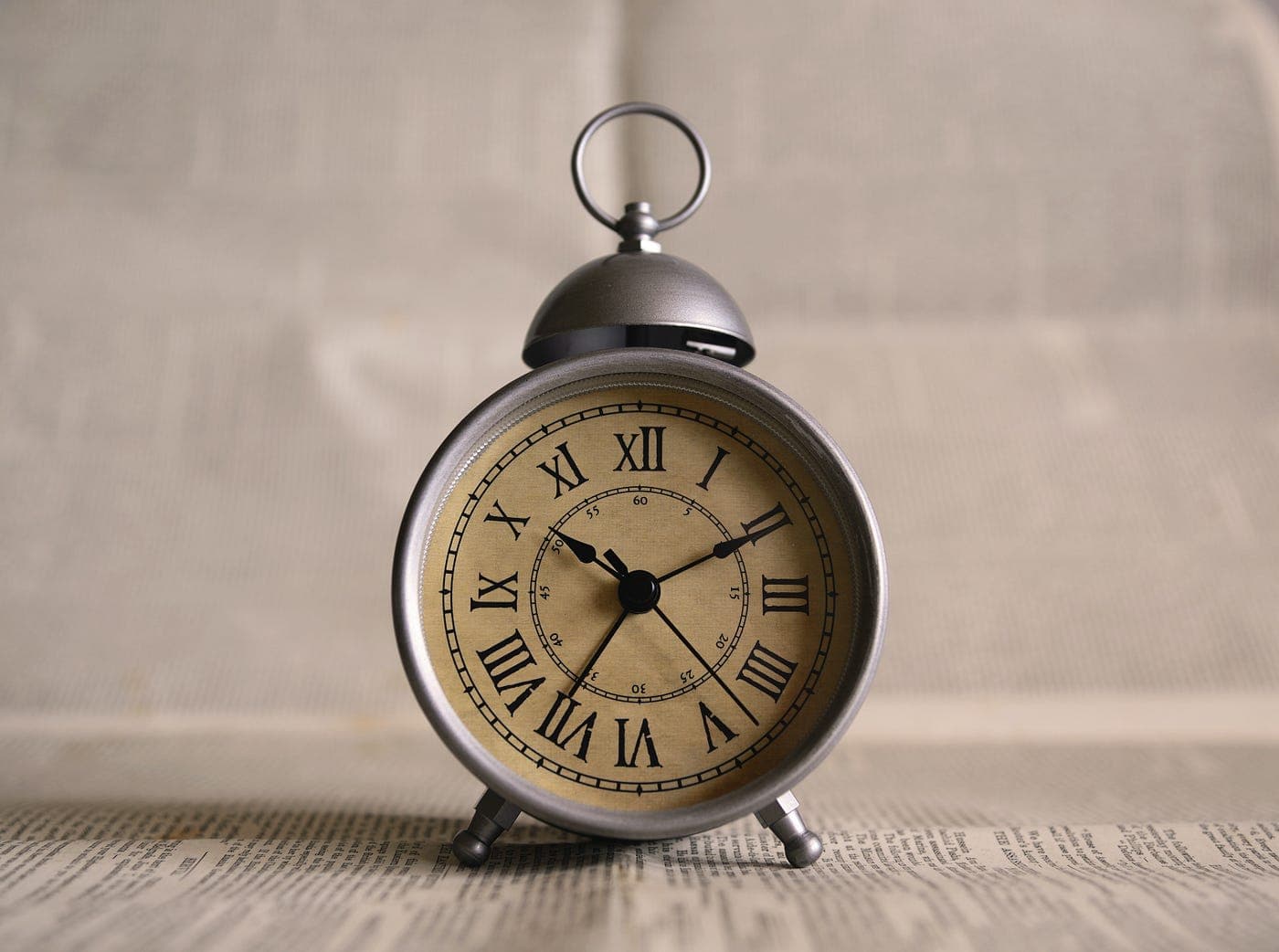 A small alarm clock sitting on top of a wooden table next to a sheet of paper with writing on it