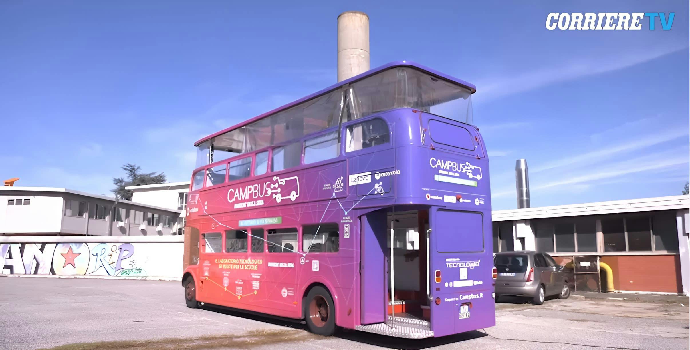 A purple double decker bus parked in a parking lot next to a building with graffiti on the side of it